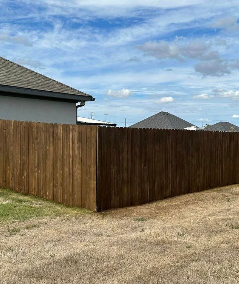 A wooden fence surrounds a house in a residential area.