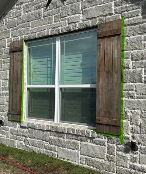 A brick wall with a window and wooden shutters painted green