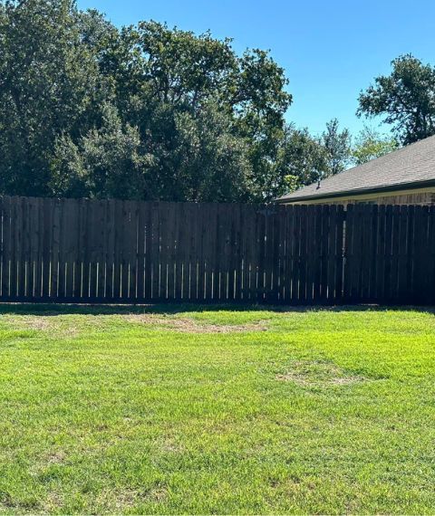 A wooden fence surrounds a lush green field in front of a house.