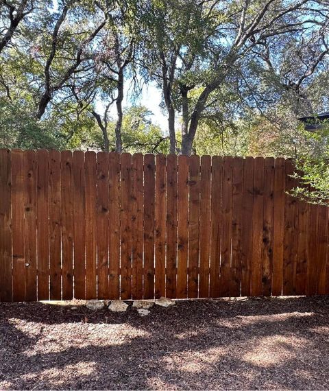 A wooden fence is surrounded by trees in a yard.