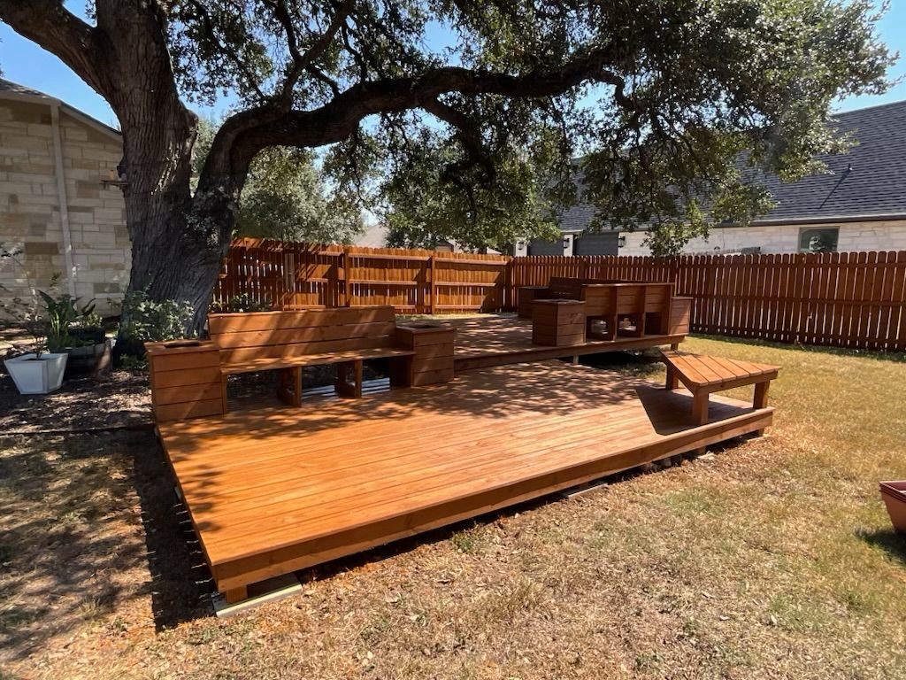 A wooden deck is sitting under a tree in a backyard.