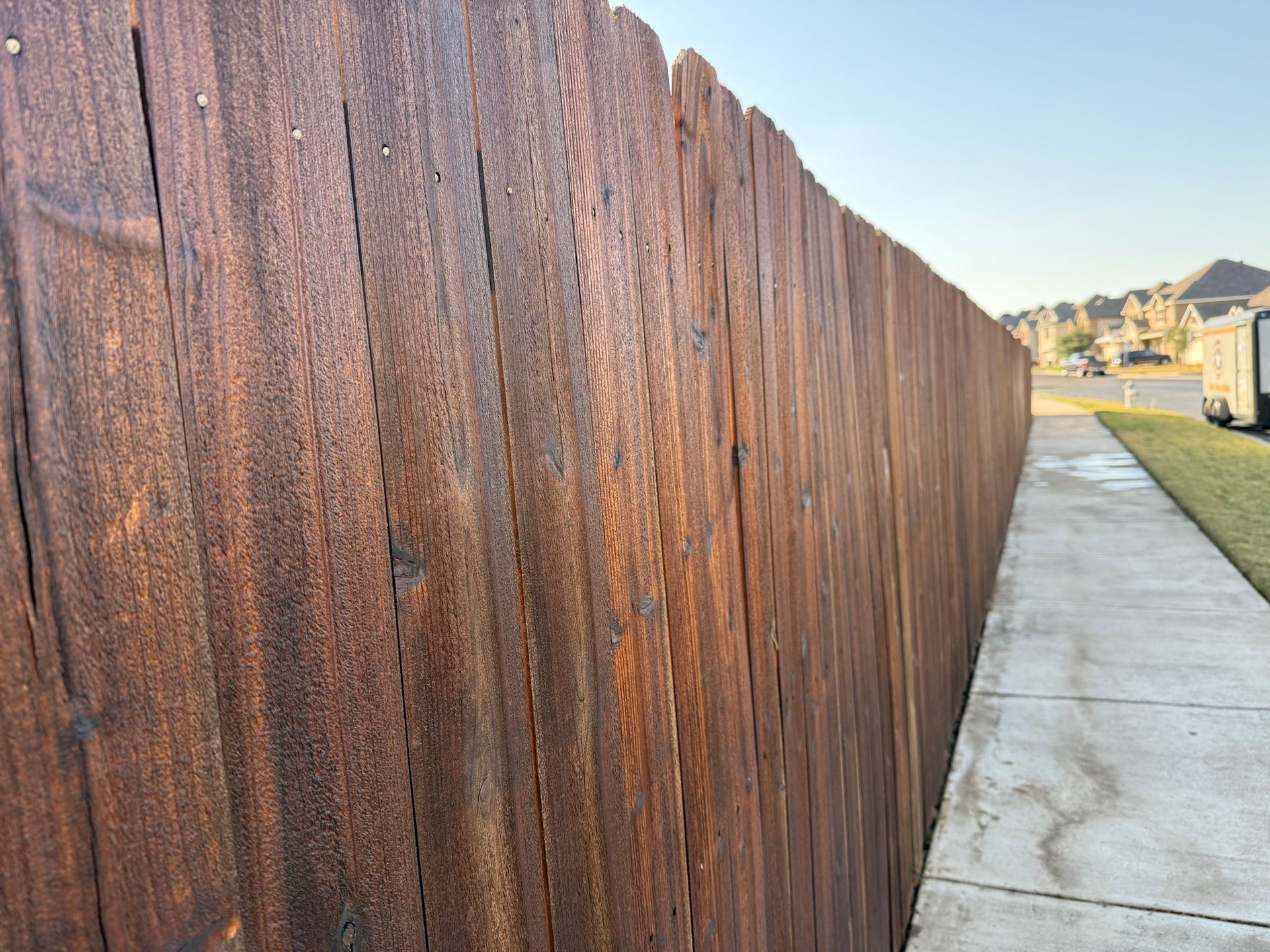 A wooden fence is next to a sidewalk in a residential area.
