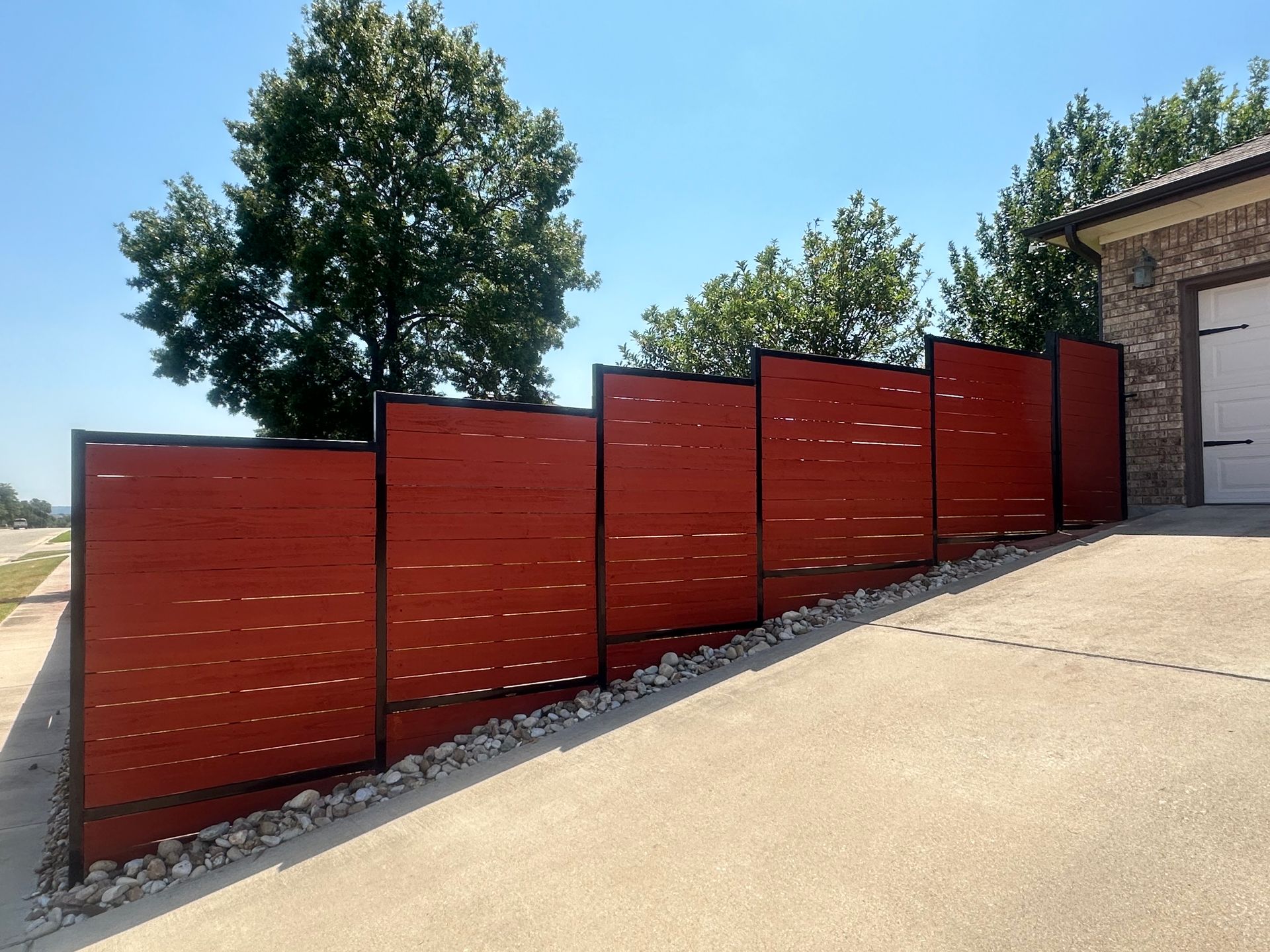 A red fence is sitting on the side of a driveway next to a garage.