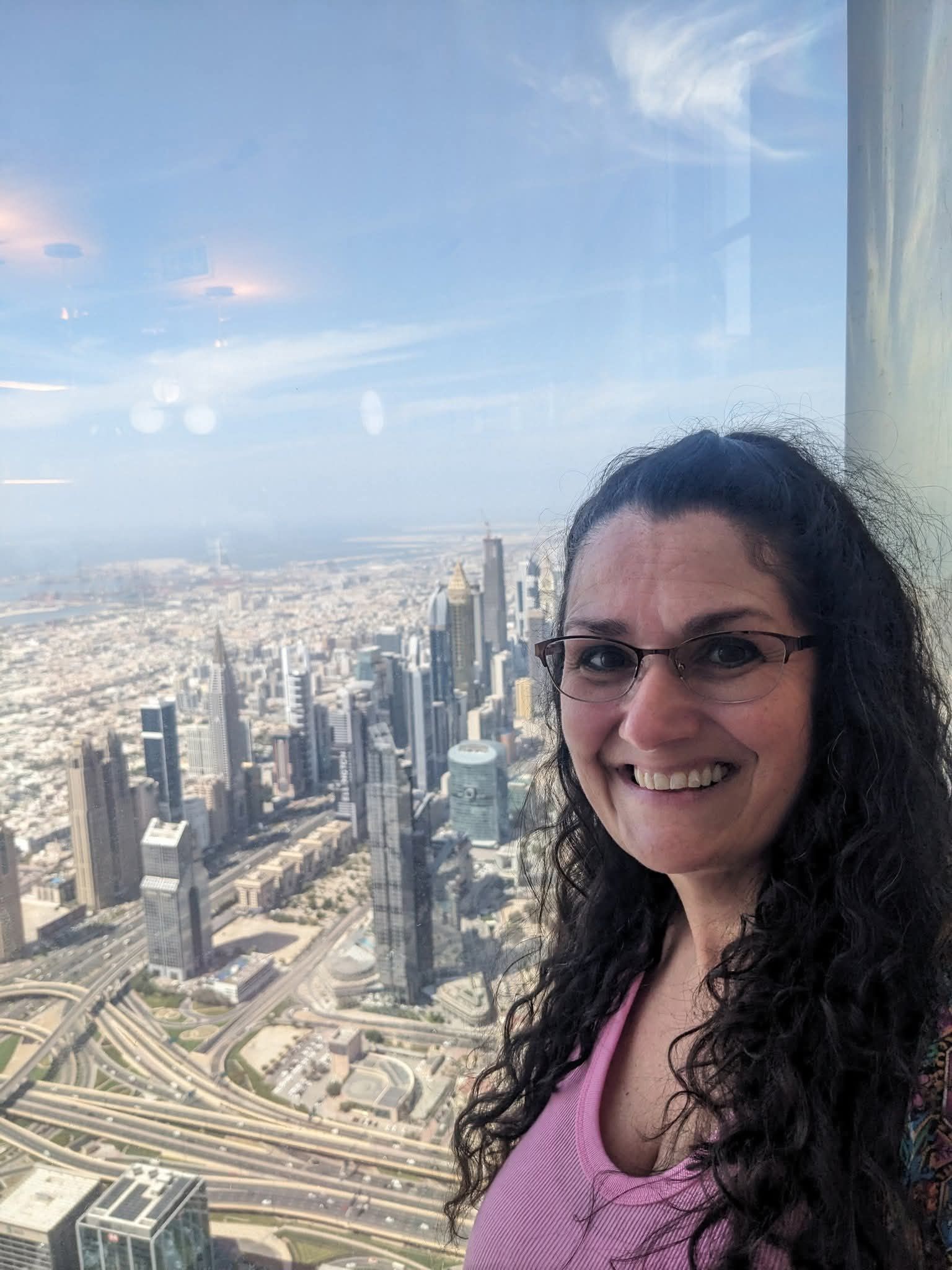 Woman smiles at the camera, city skyline visible through a window.