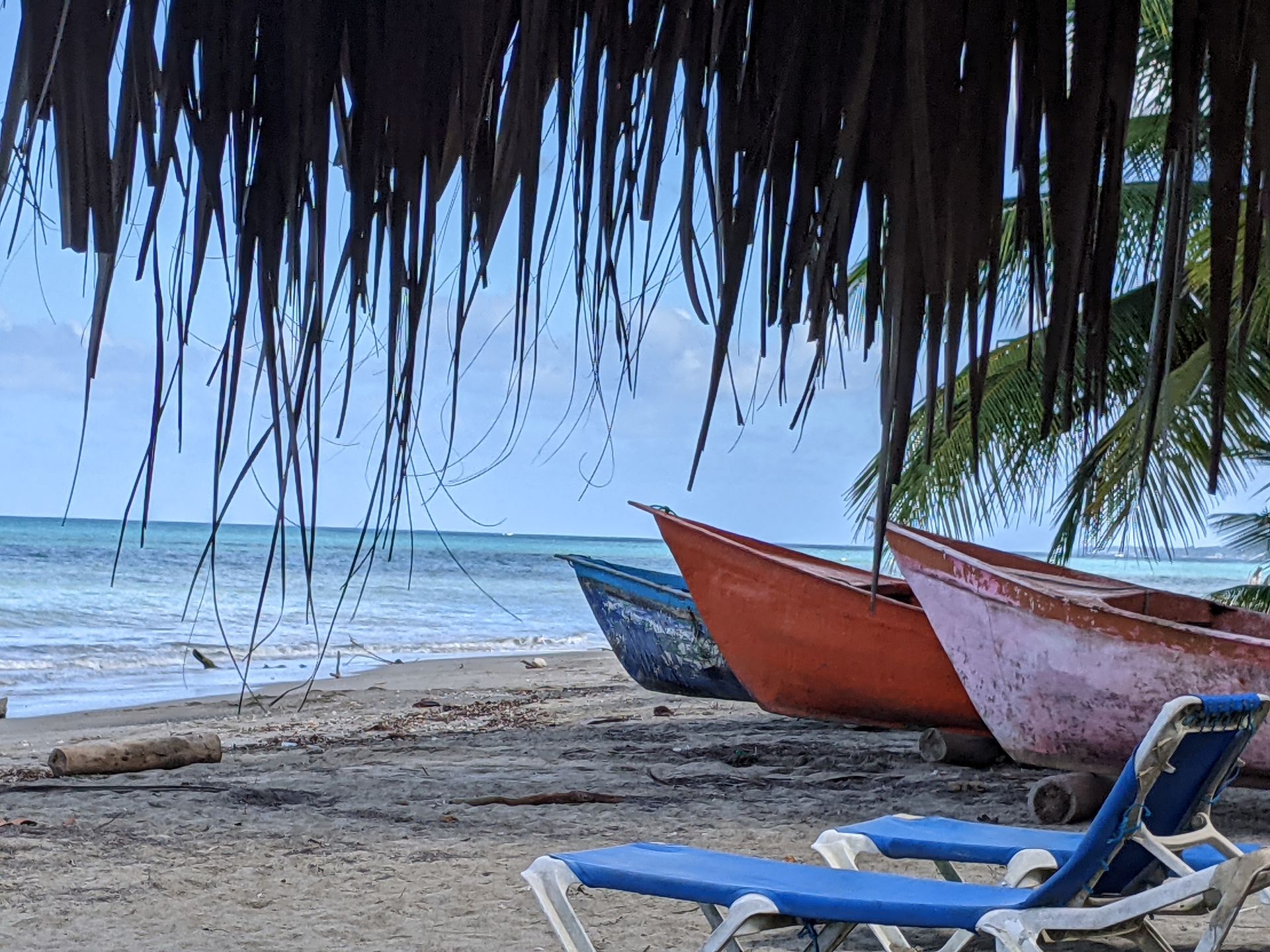 Colorful boats on a sandy beach under a thatched roof with the ocean in the background.