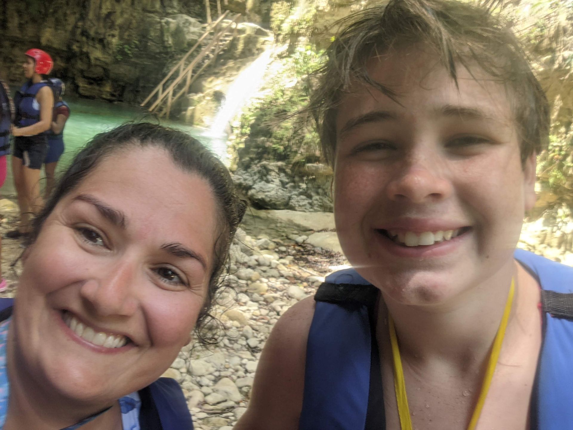 Woman and boy smiling in front of a turquoise pool, wearing life vests.