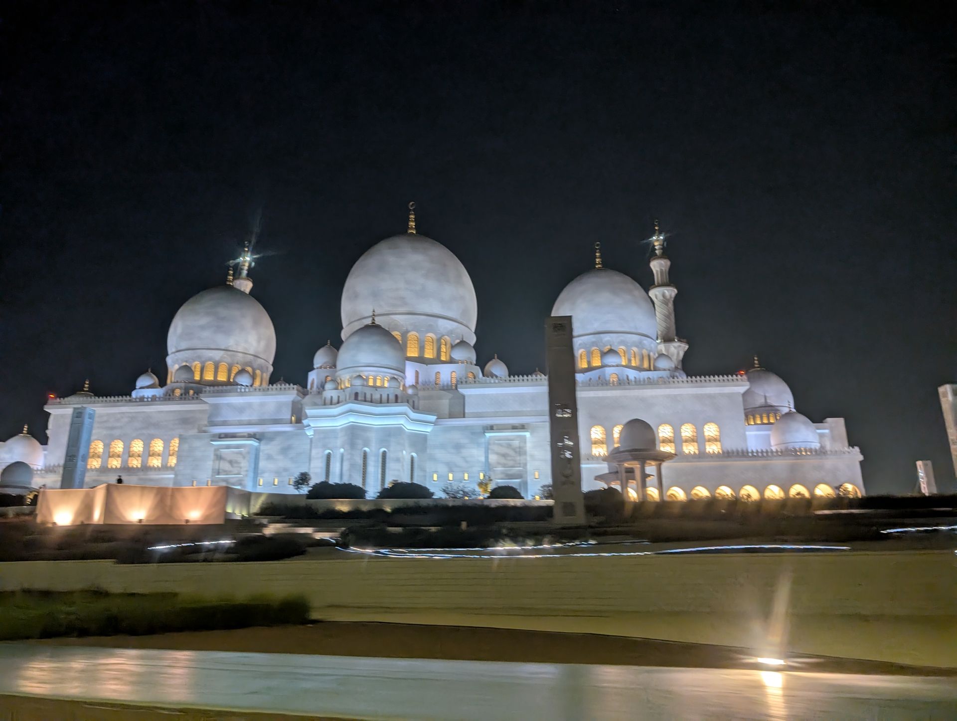 Illuminated white mosque with multiple domes and minarets against a dark night sky.