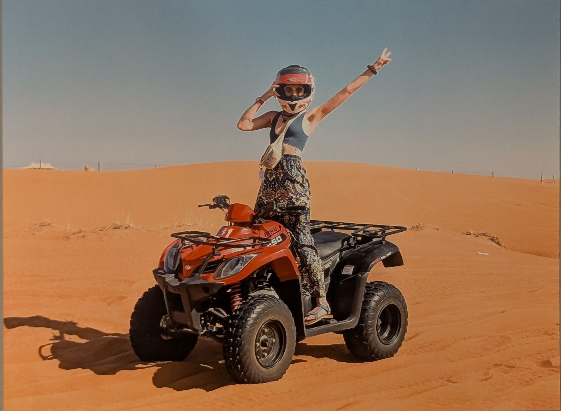 Woman on red ATV in desert, raising arm in a wave.