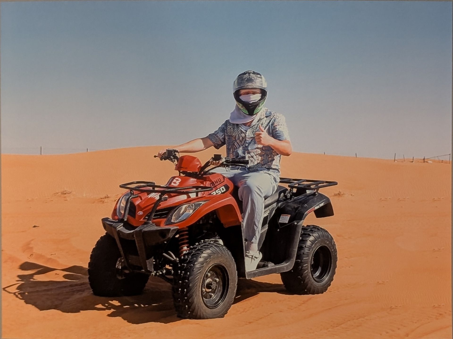 Person on a red ATV in a desert environment, wearing a helmet, giving a thumbs up.