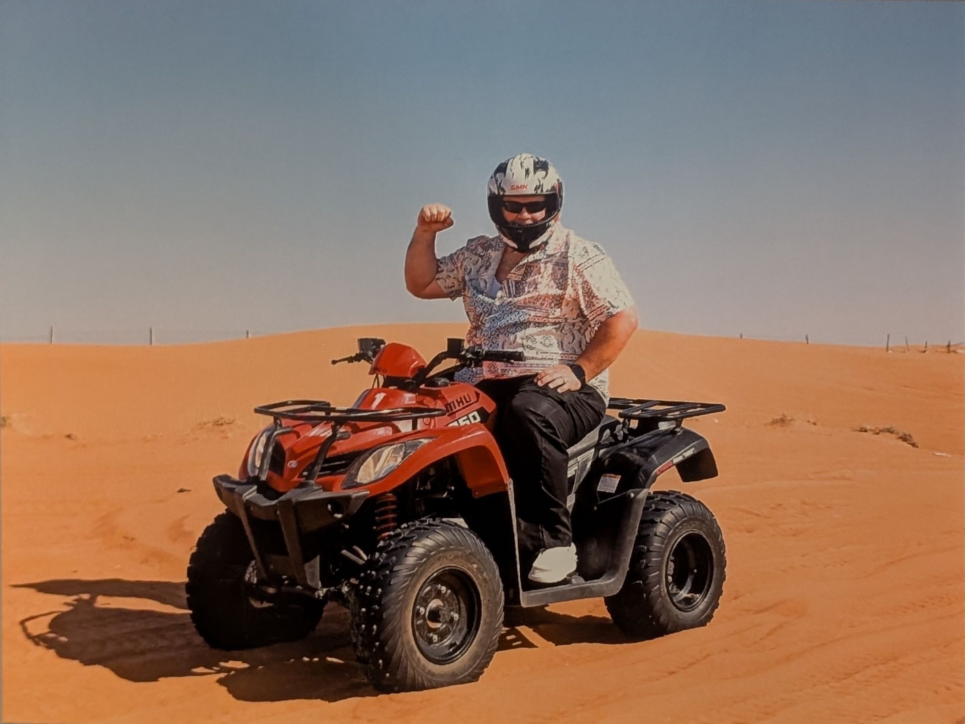 Man on red ATV in desert, raising fist.