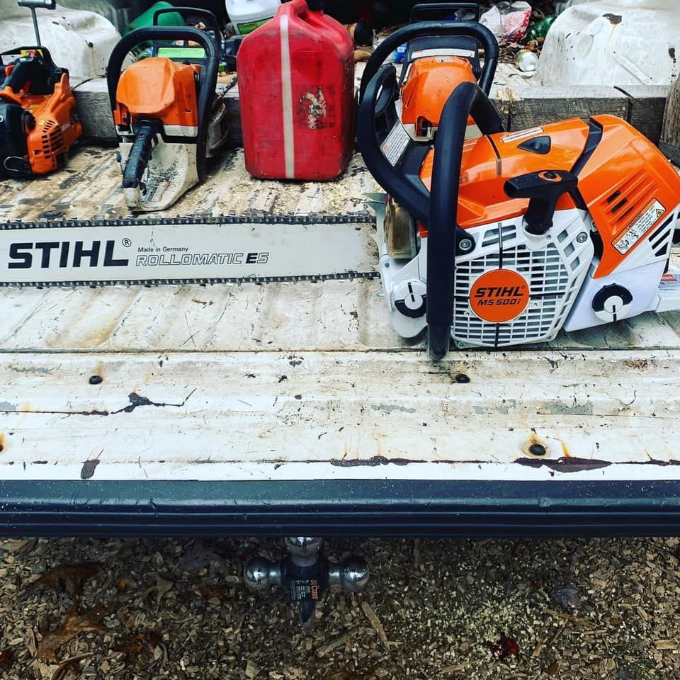 Chainsaws and gas can on a truck bed. Orange and white tools. Dark metal and wooden background.