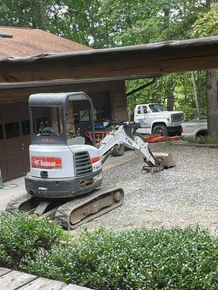 Bobcat excavator removing gravel in front of a garage, with a white truck in the background.