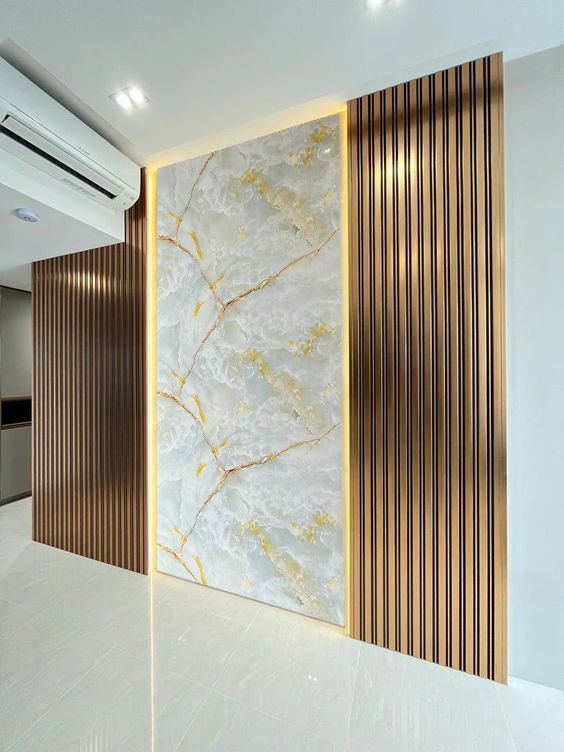 Pared interior moderna con panel central de mármol, molduras doradas y listones de madera verticales