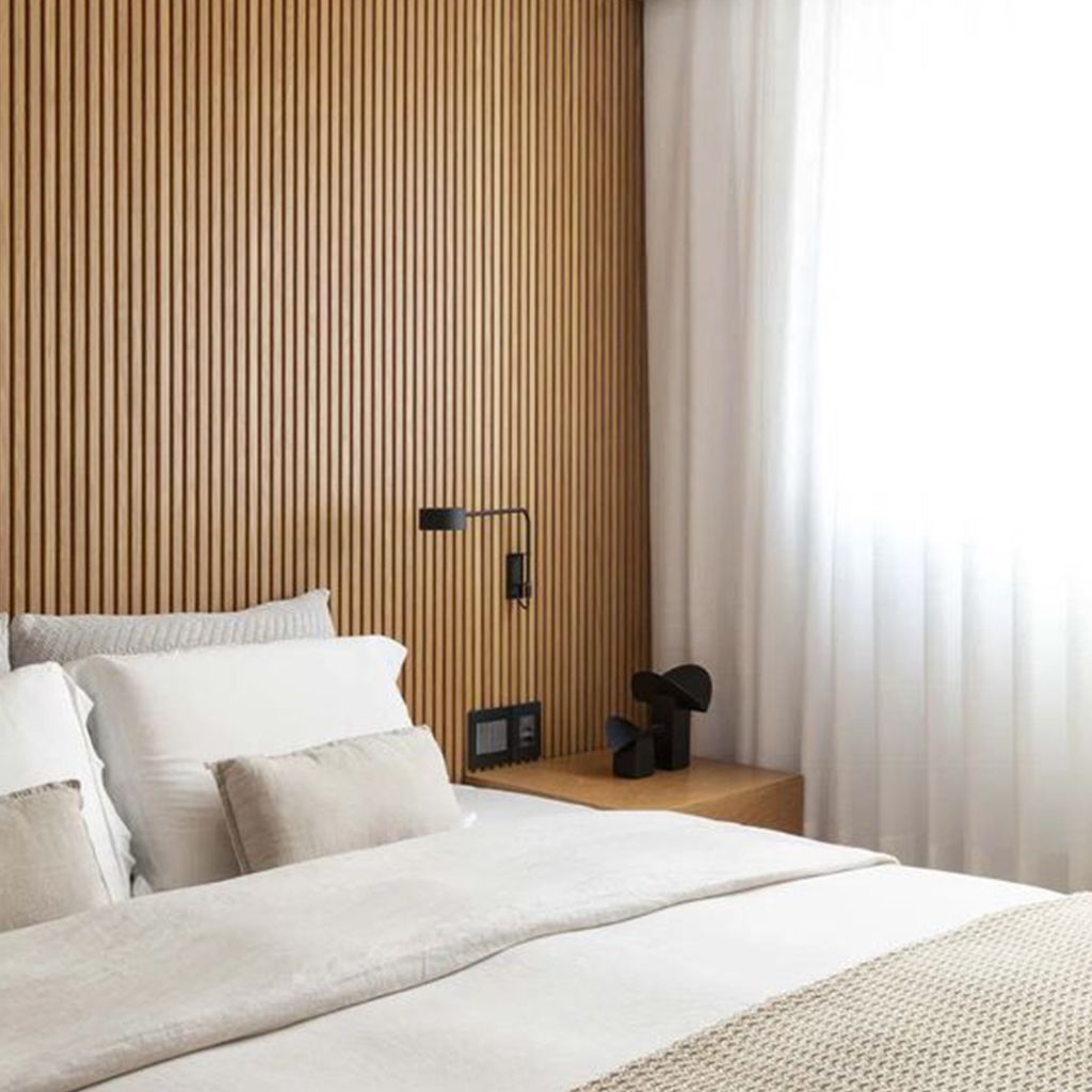 Dormitorio moderno con pared de listones de madera, mesita de noche flotante de madera y cama blanca impecablemente hecha.
