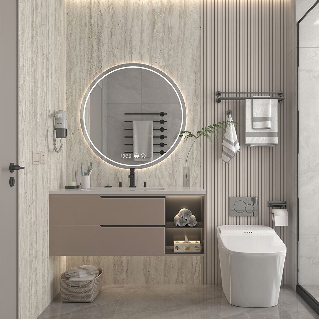 Baño moderno con espejo redondo iluminado, lavabo suspendido, papel pintado a rayas y inodoro blanco.