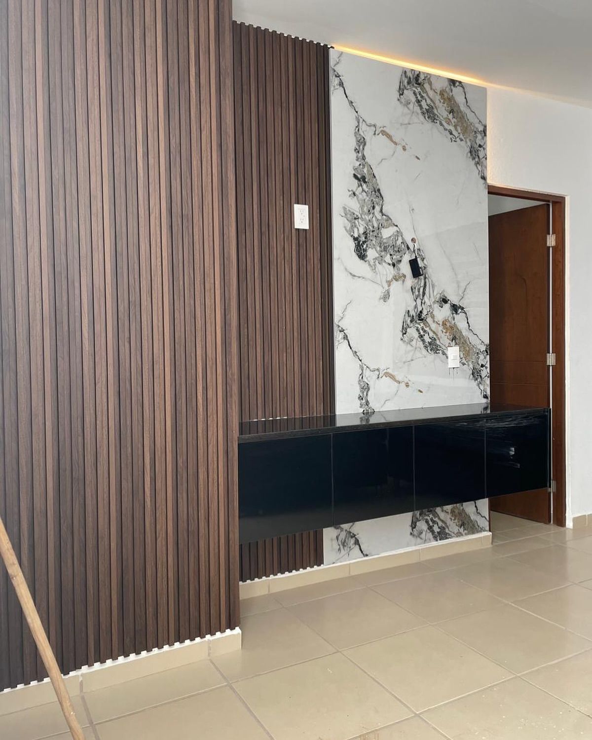 Entrada interior moderna con pared revestida de madera, panel decorativo de mármol, consola flotante negra