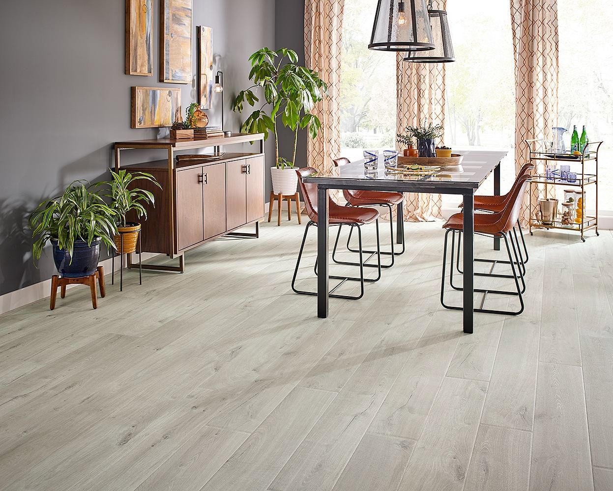 Comedor luminoso con mesa rústica, sillas, plantas y suelo de madera clara.