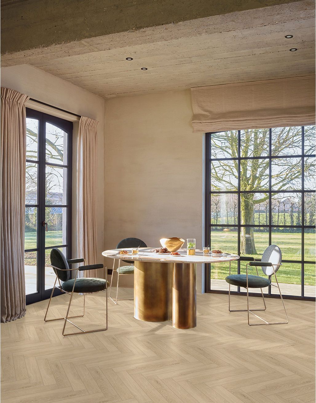 Luminoso salón con suelo de madera en espiga, mesa de comedor, plantas, escalera y aparador.