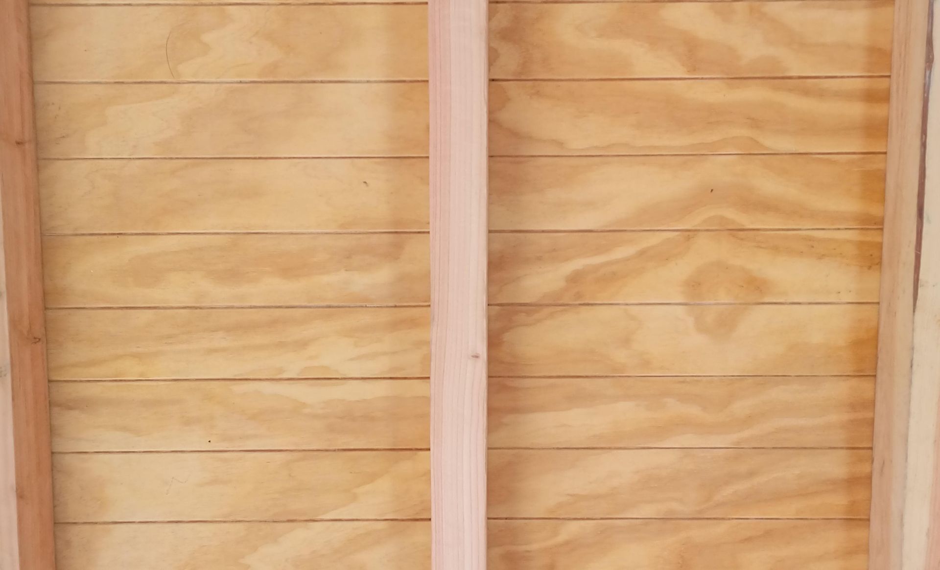 Panel alto de madera clara perforado, apoyado contra una pared de madera en un taller.
