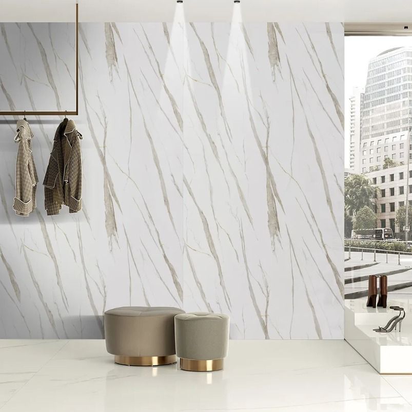 Habitación moderna y minimalista con pared de mármol blanco, detalles dorados, dos taburetes y perchero junto a la ventana.