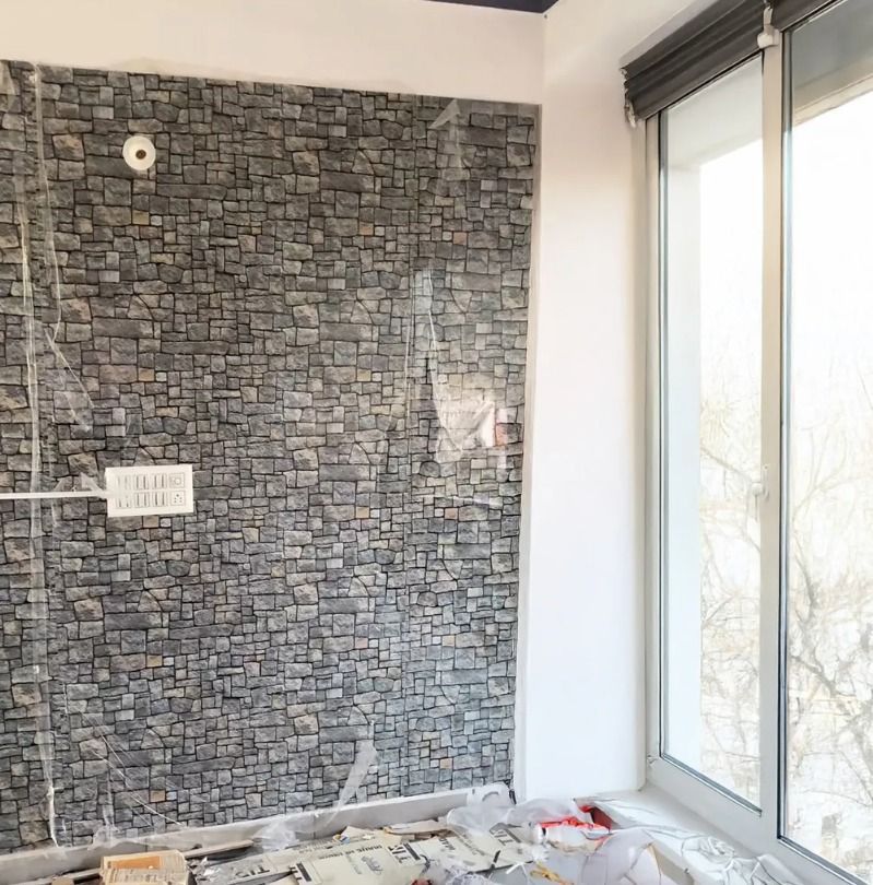 Escena de decoración interior con silla de mimbre, plantas en macetas y jarrones blancos contra una pared de piedra.
