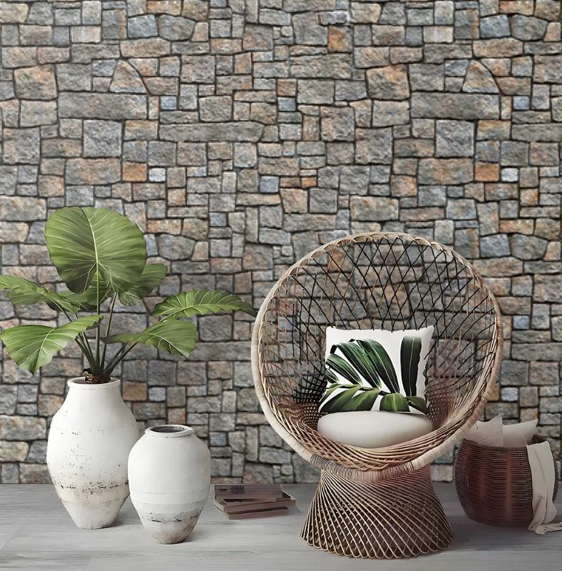 Escena de decoración interior con silla de mimbre, plantas en macetas y jarrones blancos contra una pared de piedra.