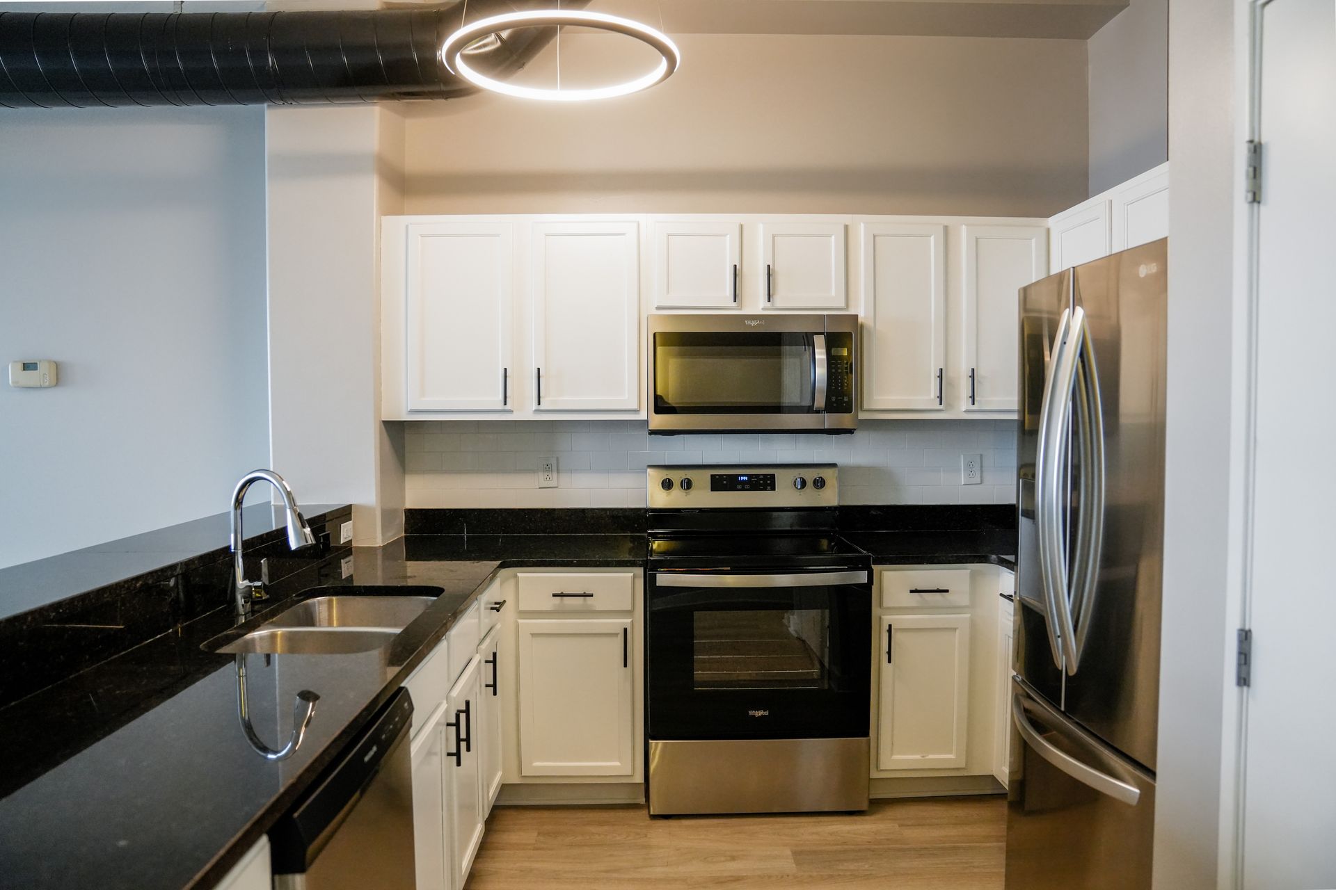 A kitchen with white cabinets , stainless steel appliances , a sink , and a refrigerator.