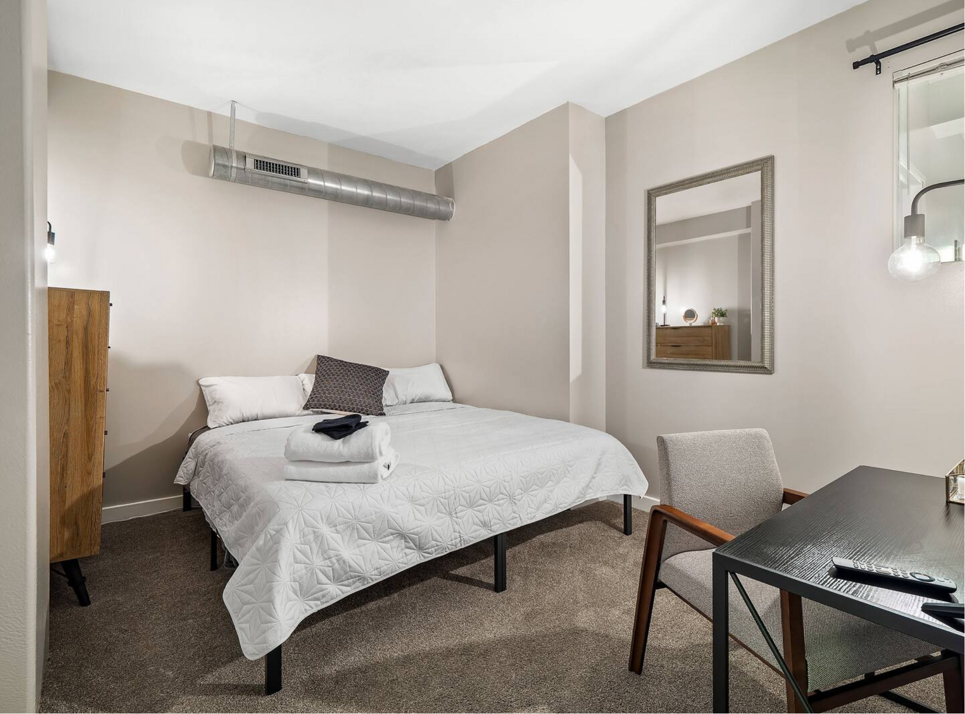 A bedroom with a bed , chair , desk and mirror.