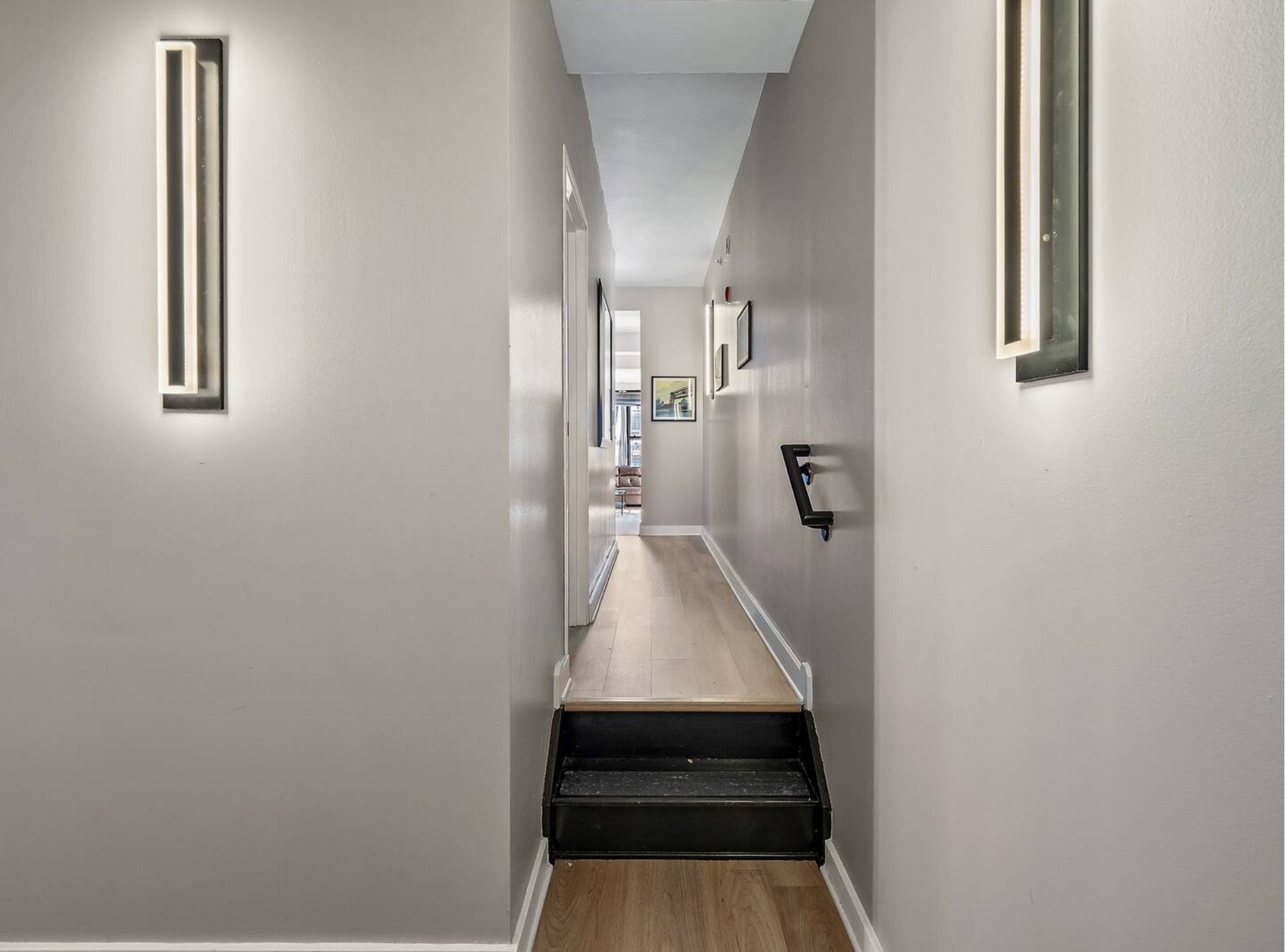 A long hallway with wooden floors and stairs leading to a living room.