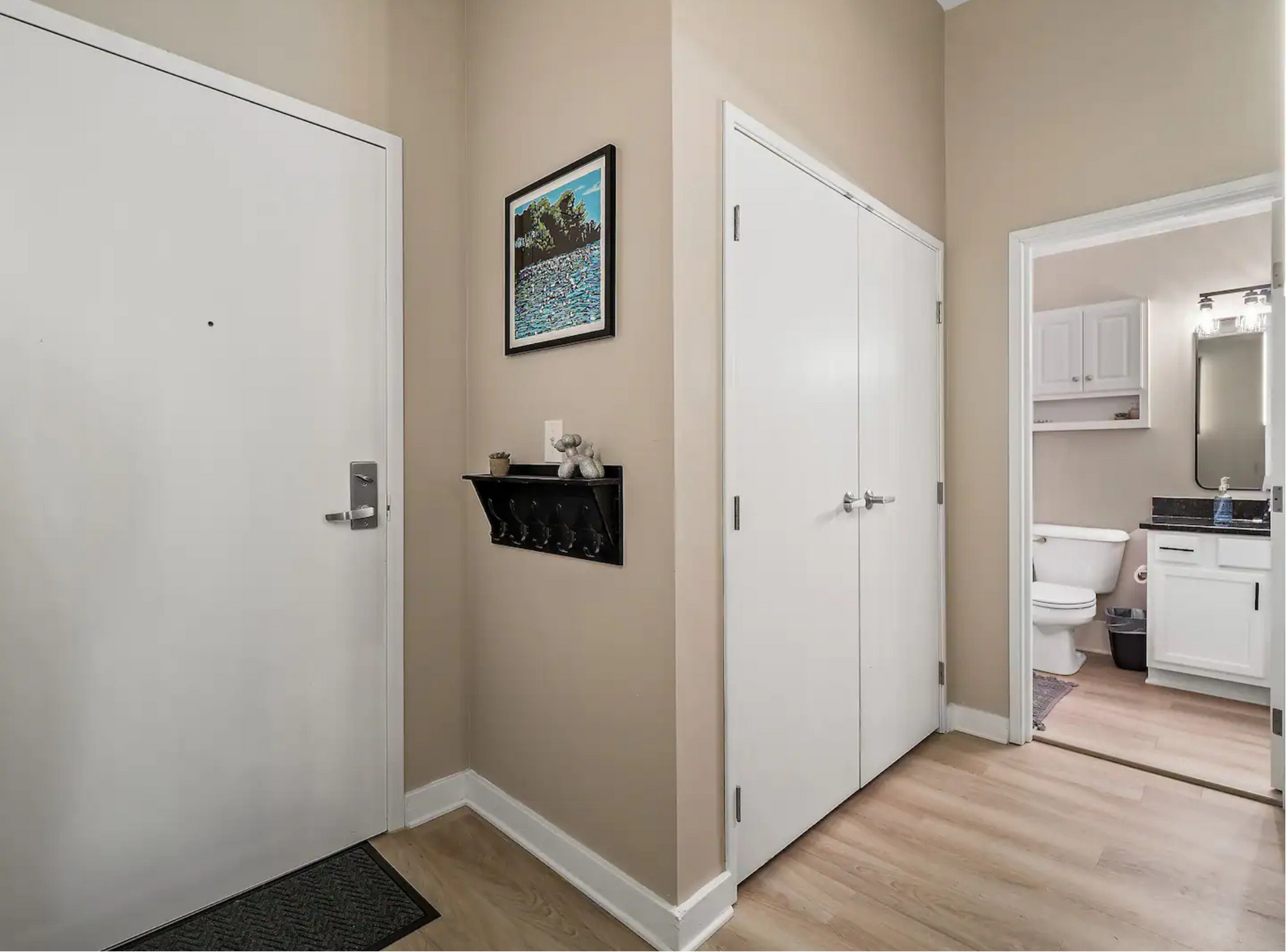 A hallway with a picture on the wall leading to a bathroom.