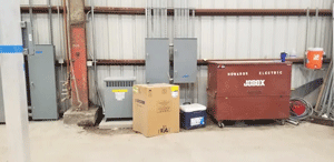 Warehouse interior with electrical boxes, a large red tool chest, a cardboard box, and a cooler.