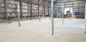 Interior of a large warehouse with metal beams and a concrete floor.