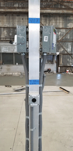 Electrical conduit and boxes mounted on a silver support beam, in an industrial setting.
