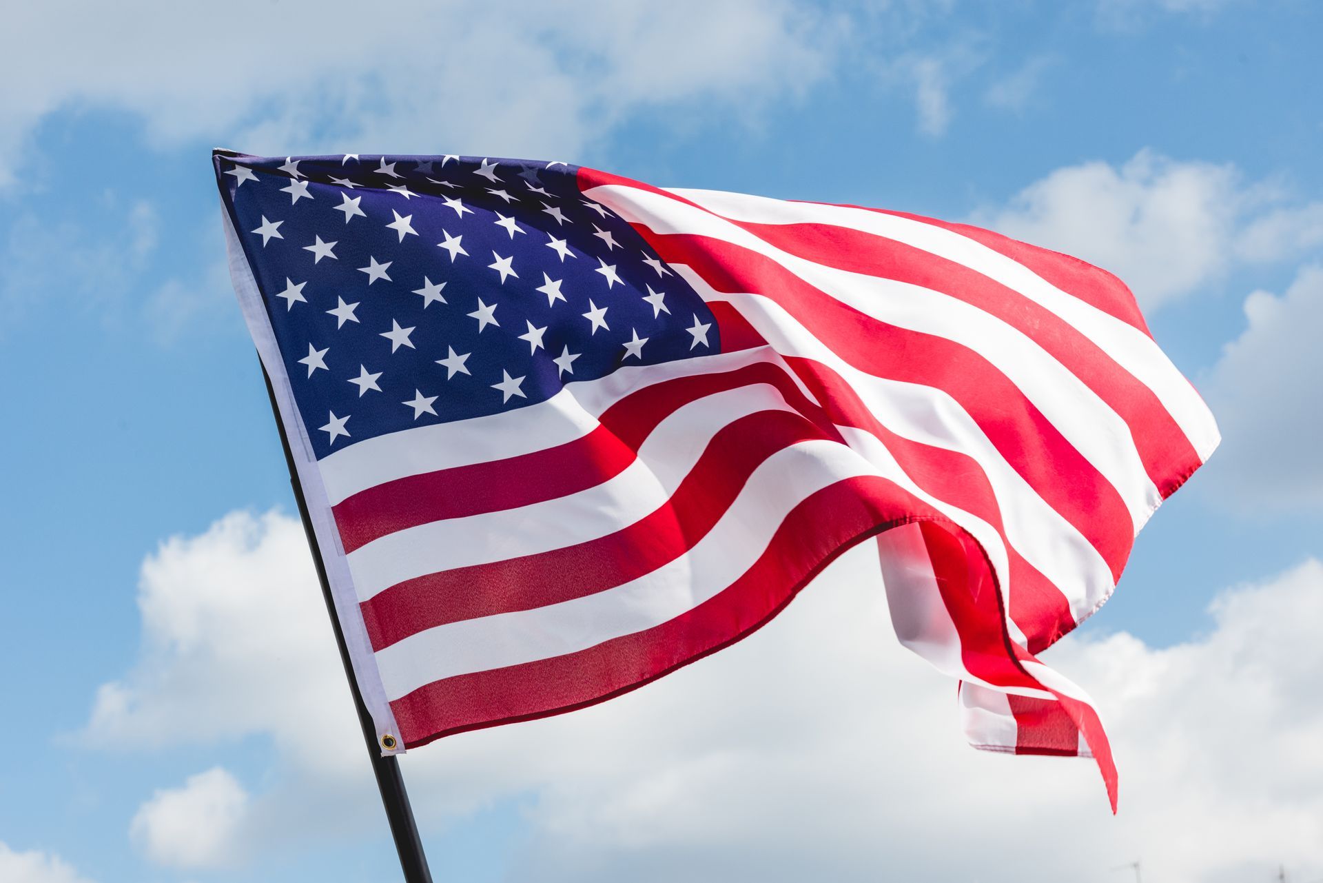 American flag waving against a blue sky with clouds