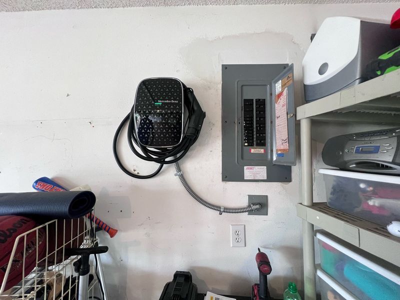 An electric vehicle charger and electrical panel mounted on a white garage wall.