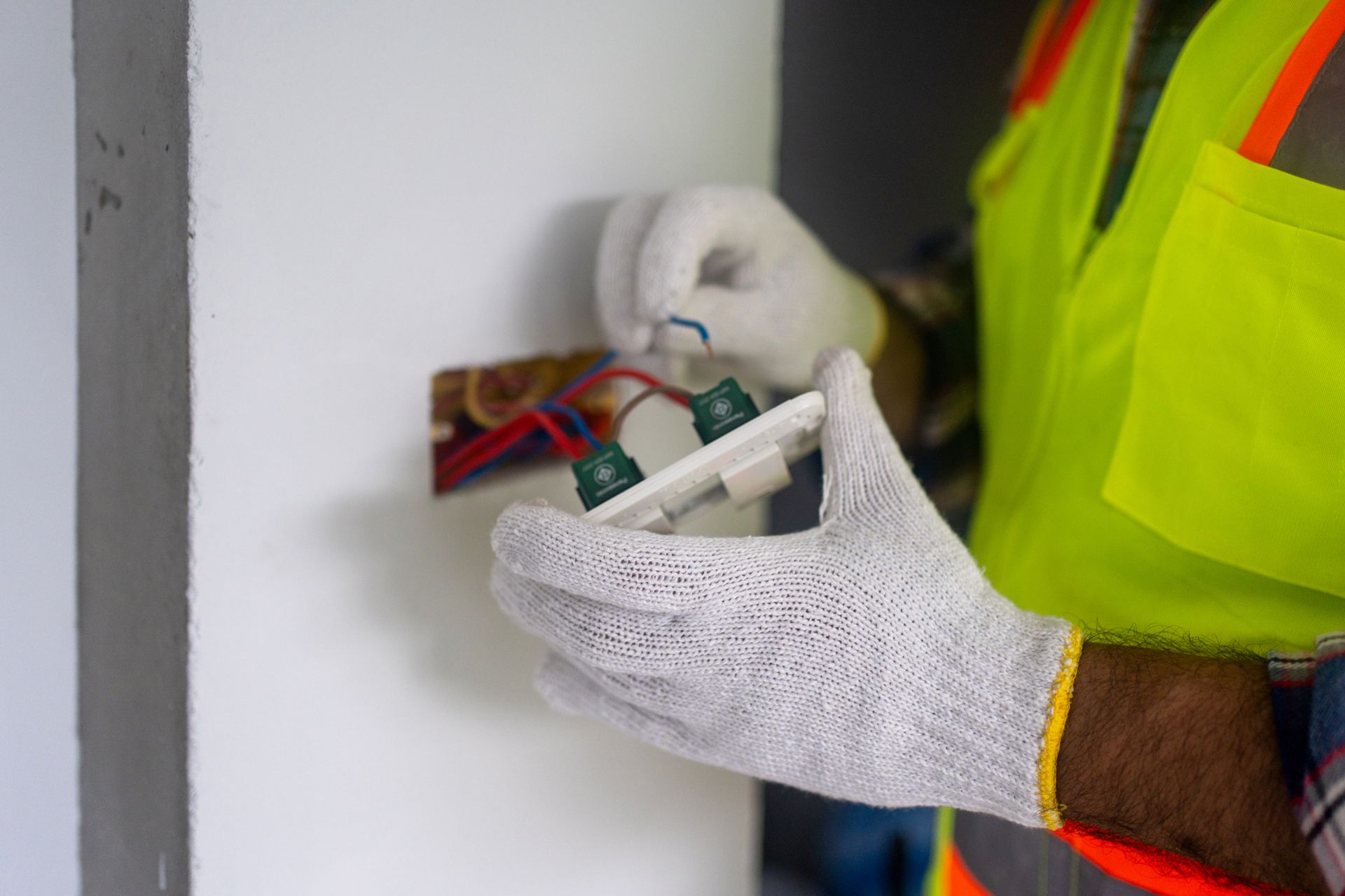 Electrician installing a light switch, wearing a safety vest and gloves.