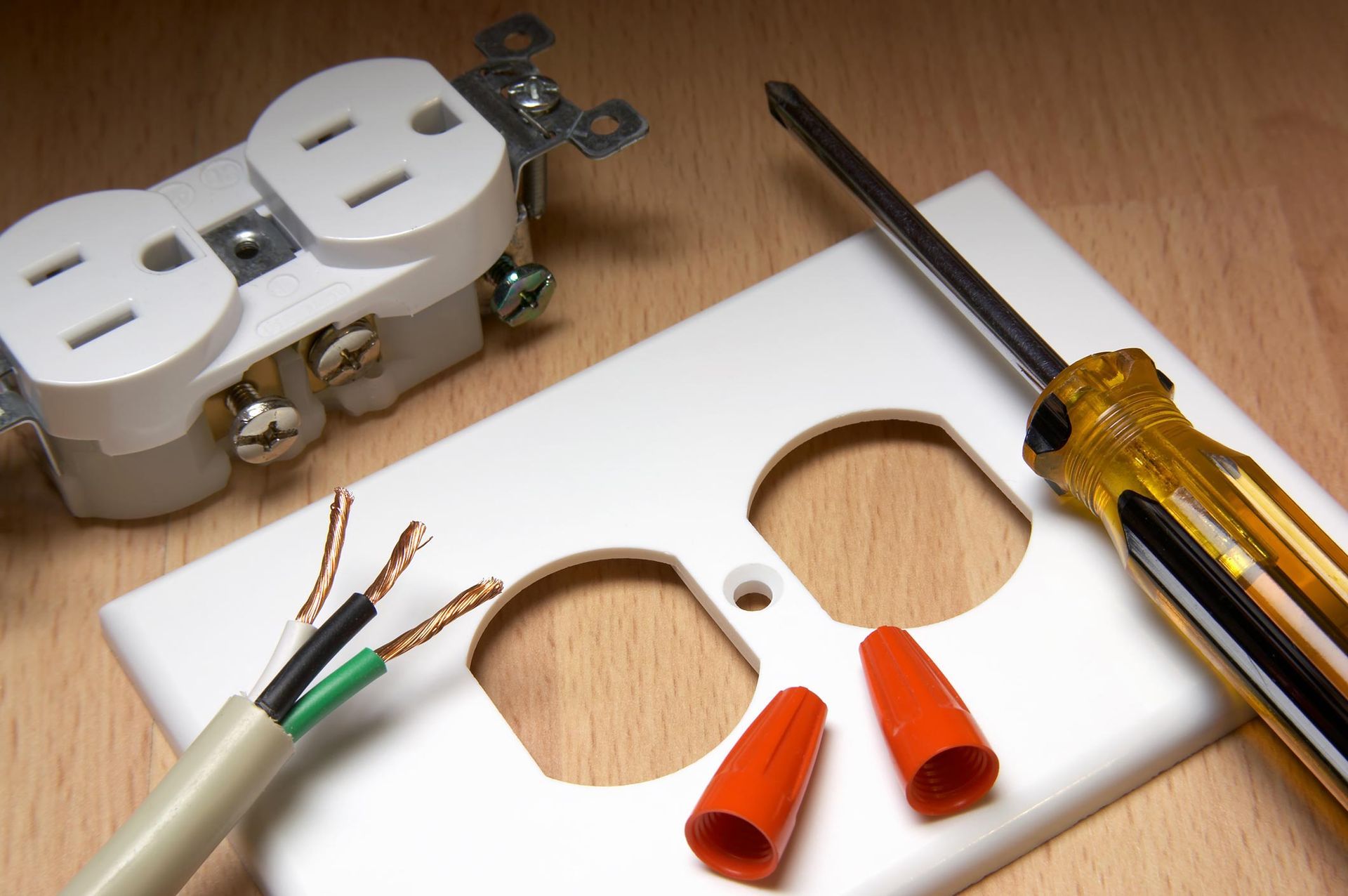 Electrical outlet repair: outlet, wires, screwdriver, orange wire connectors, and faceplate on wood.