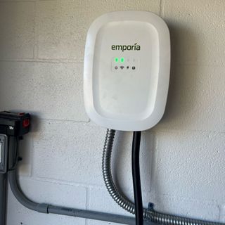 White Emporia EV charger mounted on a brick wall. Black charging cable extends from bottom.