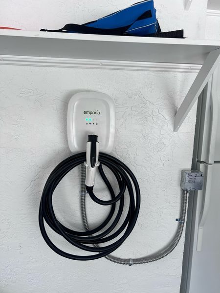 EV charger, black box, and electrical panel mounted on a white wall. Gray conduit connects components.