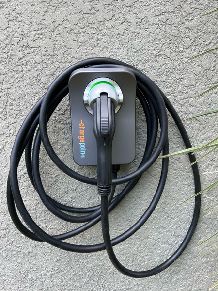 Electric vehicle charger mounted on a textured, light-colored wall with its cable coiled around it.