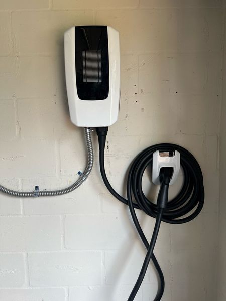 White EV charger mounted on a white brick wall, with a coiled charging cable hanging nearby.