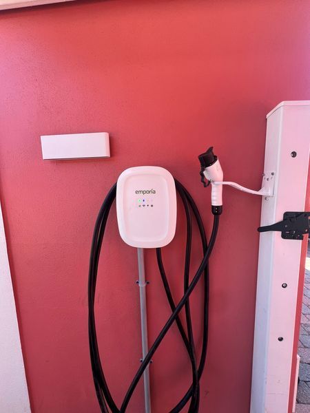 Electric vehicle charger on a red wall. White charger with black cable and plug on right.