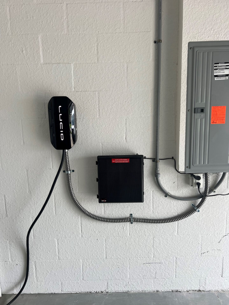 EV charger and electrical panel mounted on a white painted brick wall. Black charger is branded