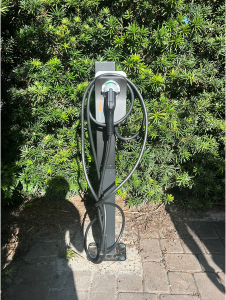 EV charging station with cable, set against a green hedge.
