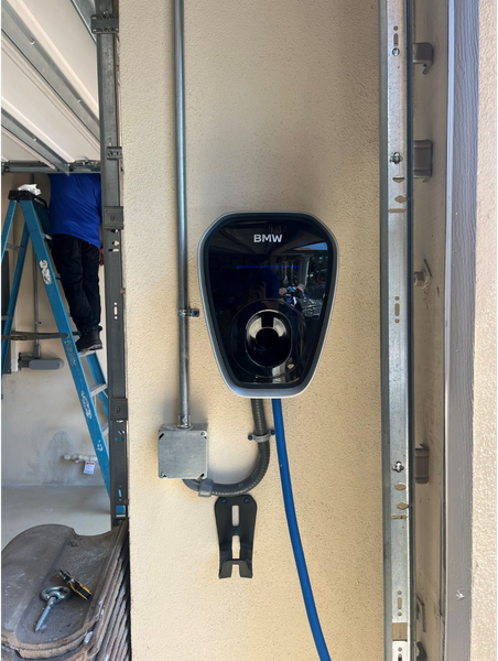Electric vehicle charger installed on a beige wall in a garage. An electrician works nearby.