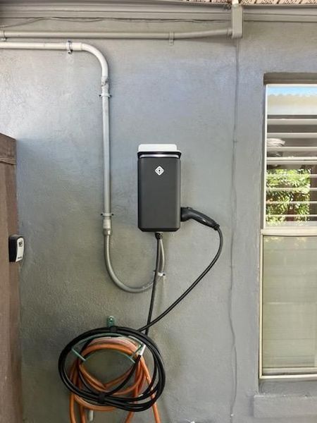 Electric vehicle charger mounted on a gray wall with conduit and a coiled charging cable.