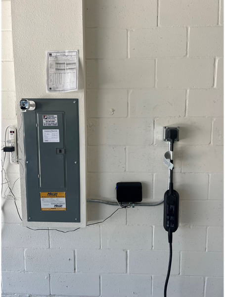 Electrical panel, EV charger, and conduit mounted on a white brick wall.
