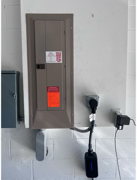 Electrical panel and EV charger on a white wall. Gray panel, black charger, and black cable are visible.