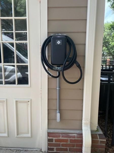 Black EV charger mounted on tan building exterior next to a door and white downspout.