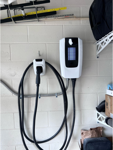 White electric vehicle charger mounted on a brick wall with charging cable.